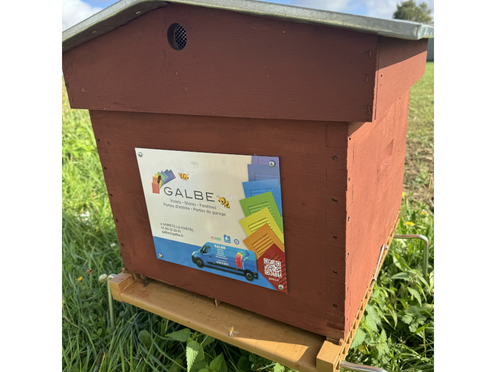 Ruche Apihappy en bois rouge portant la plaquette signalétique d'une entreprise partenaire